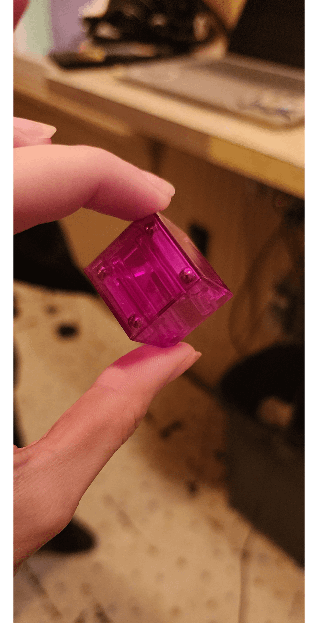 ​1″ x 1″ x 1″ cube made of strong magenta plastic with metal balls in the corners