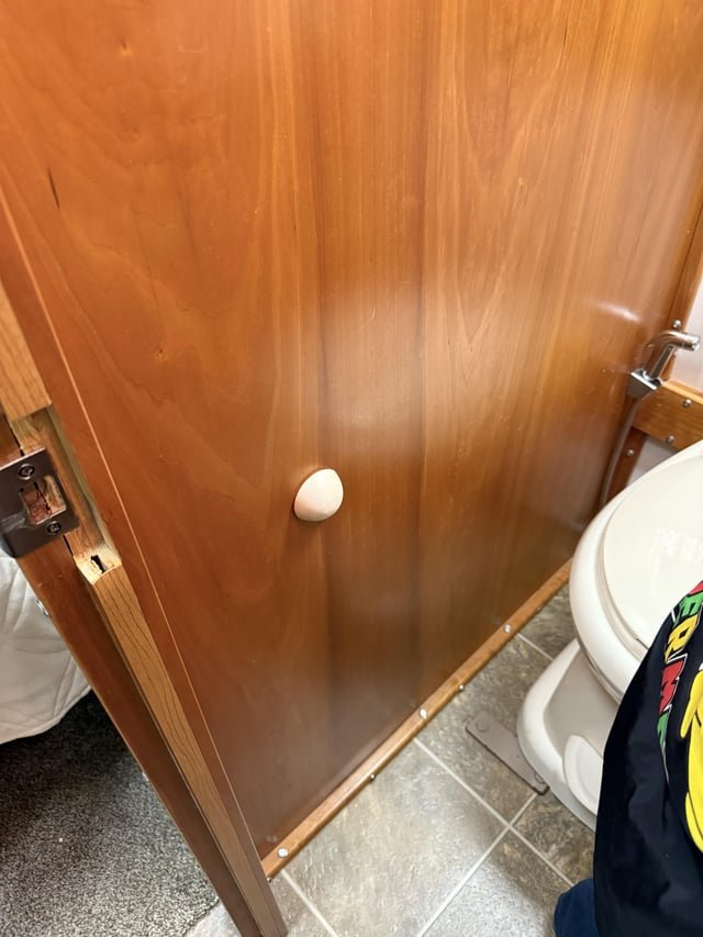 ​White dome shaped object on the wall of a RV bathroom. Not to stop the door- it opens the other way.