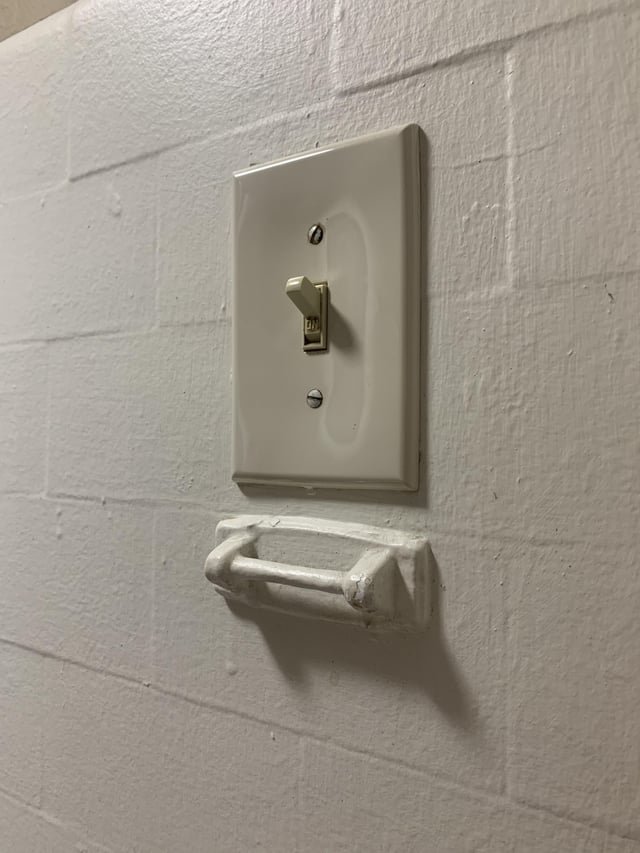 Small white ~3 inch metal bar, looks like a mini towel rack below light switch in bathroom in my apartment. Building is 105 years old, in US. Attached to wall with ceramic. Also attached to wall is a soap holder and what looks like a cup holder made of same ceramic material, both near the sink.