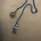 ​two metal charms (an owl on a branch and a seal of some sort) on either end of a blue fabric cord, about 14 inches long