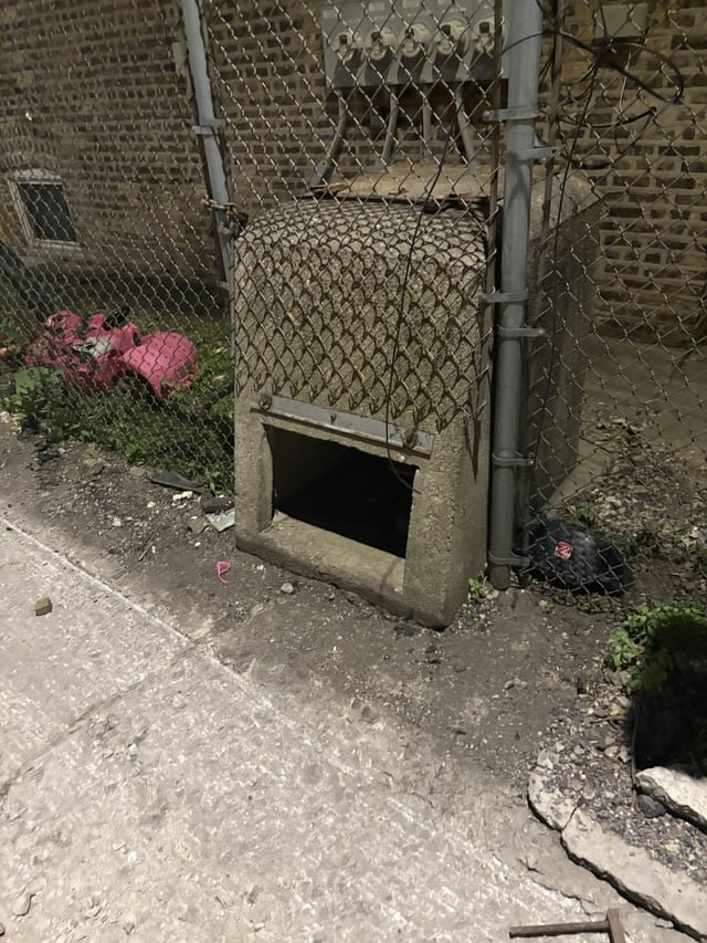 Concrete box with a small opening sticking out of a chain link fence, Chicago IL