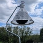 ​Spherical black object covered by a conical mesh net, with a liquid container up top, about 7ft / 2m tall. Seen at a wildlife park