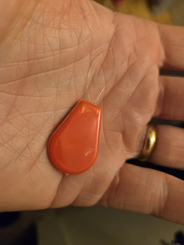 ​Red plastic teardrop thing with a thin metal wire loop on the end. Injection molding marks around the edge but otherwise blank